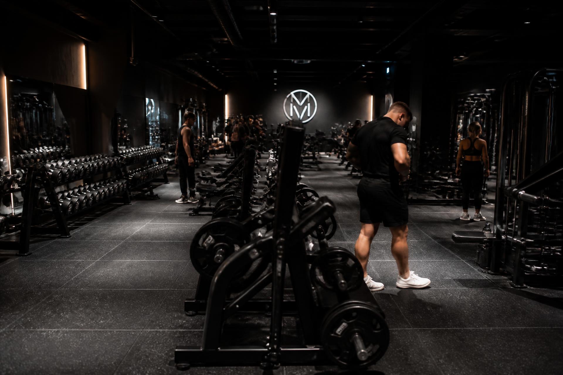 Área de musculação da academia com equipamentos e alunos treinando